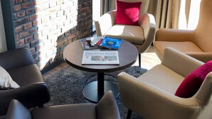 A modern lounge area with leather armchairs, a round coffee table with magazines, and a brick wall. - Rafaela Hotel Heidelberg (Heidelberg)