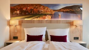A hotel room with a large bed, two pillows, a red blanket, and a painting of a scenic landscape above the bed. - Rafaela Hotel Heidelberg (Heidelberg)