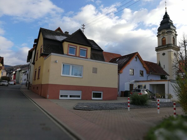A two-story building with a garage, a church with a clock tower, and a clear sky.