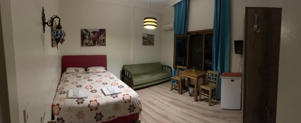 A bedroom with a bed, a green sofa, a small table with chairs, a desk, and a refrigerator.