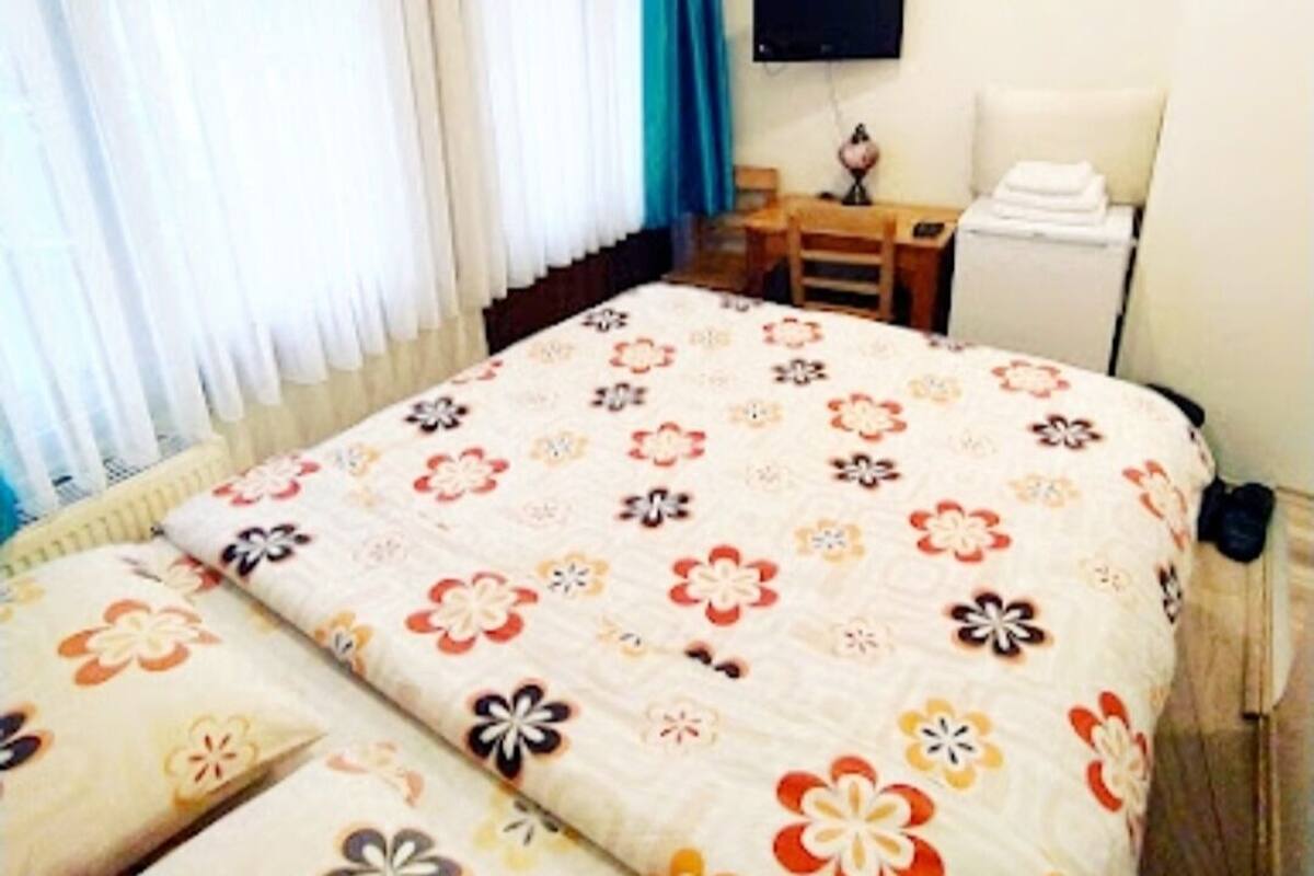 Habitació d'hotel amb llit, escriptori, cadira, televisió i finestra amb cortines.