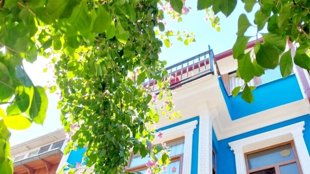 A hotel facade with a blue and white color scheme, a balcony with red curtains, and an air conditioning unit. - Halikarnas Butik Hotel (Adalar)