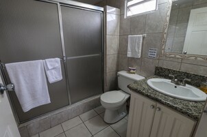 Baño con ducha, inodoro, lavamanos y un cartel solicitando el uso de toallitas para maquillaje.