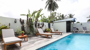 A poolside area with lounge chairs and a small building, likely a shower room, with a tiled pool.