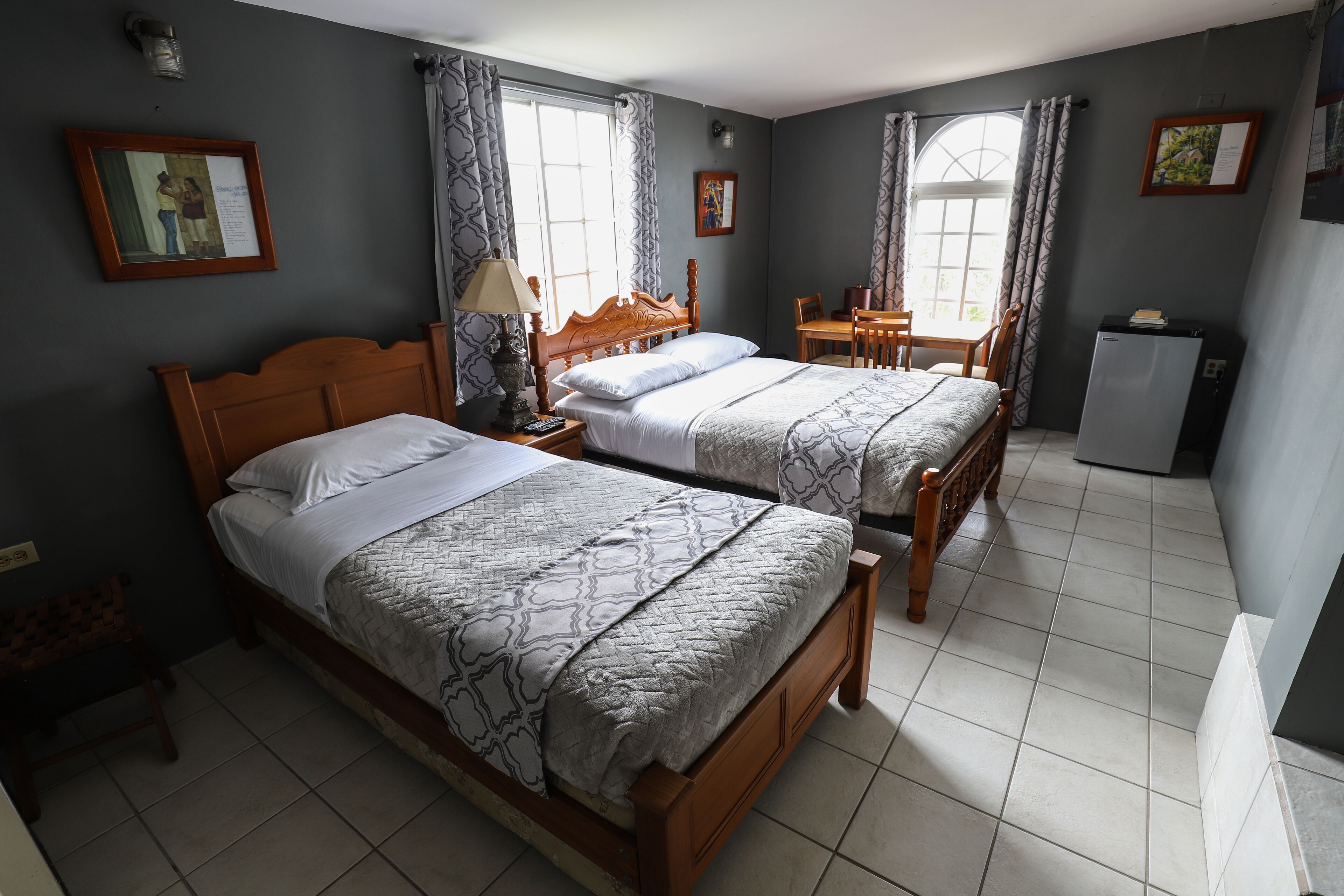 A hotel room with two wooden beds, a small table, and a refrigerator.