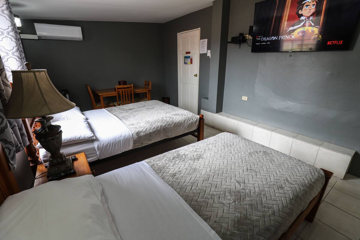 A hotel room with two beds, a desk, a chair, a lamp, and a TV displaying 'The Dragon Prince' on Netflix.