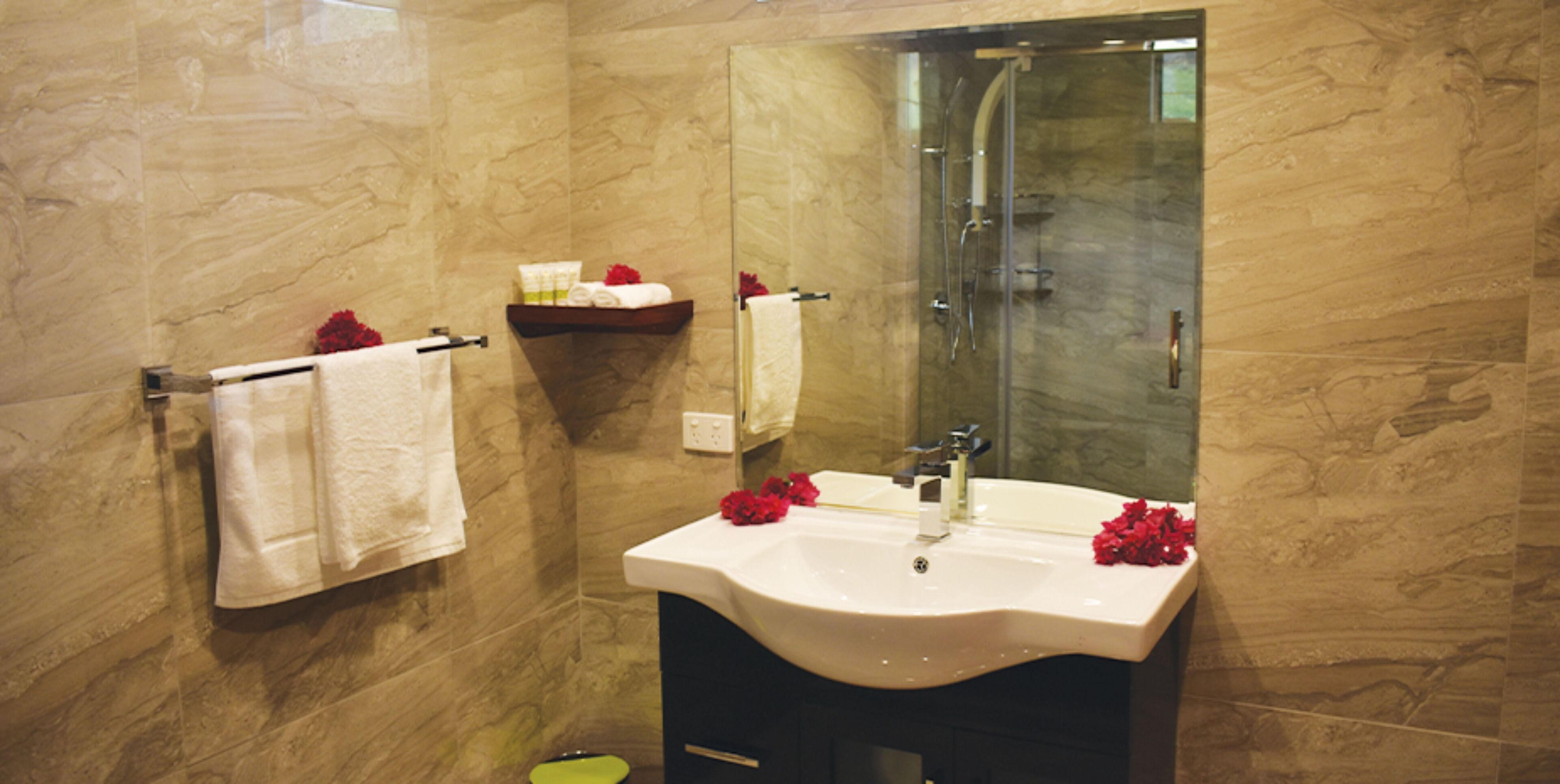 A bathroom with a marble wall, a white sink, and a glass shower enclosure.