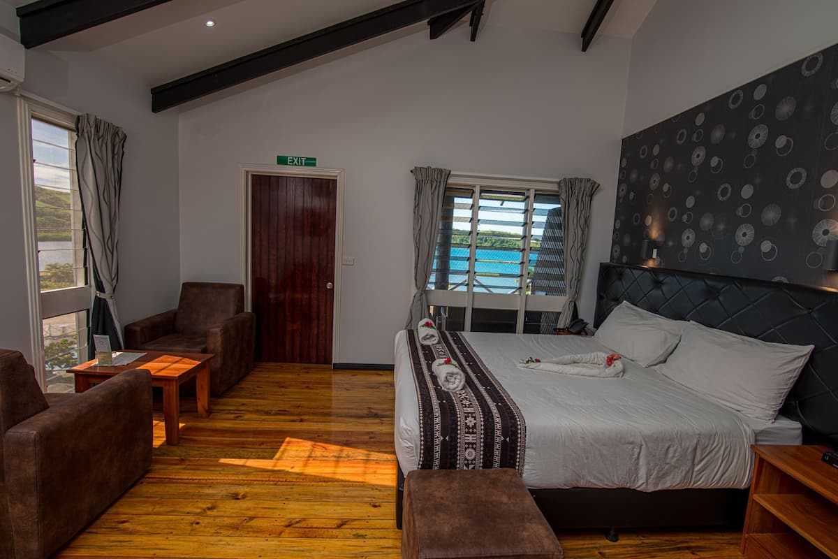 A hotel room with a bed, a sofa, a wooden floor, a window with curtains, and a wall with a circular pattern.