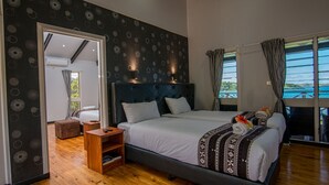 Un dormitorio con una cama grande, una mesita de noche de madera, una zona de estar pequeña y vistas al exterior a través de una ventana.