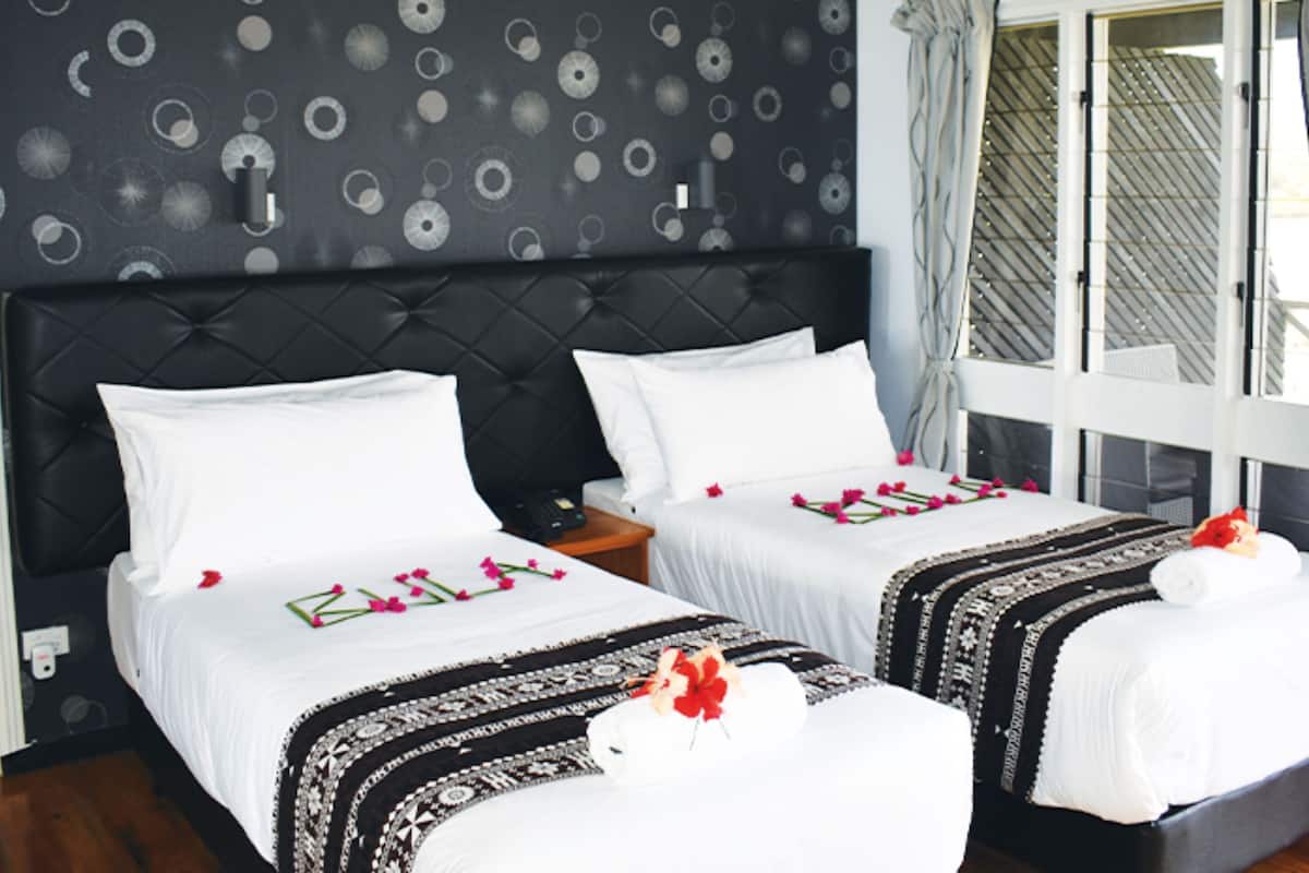 A hotel room with two beds, a dark headboard, a patterned wall, and a window with curtains.