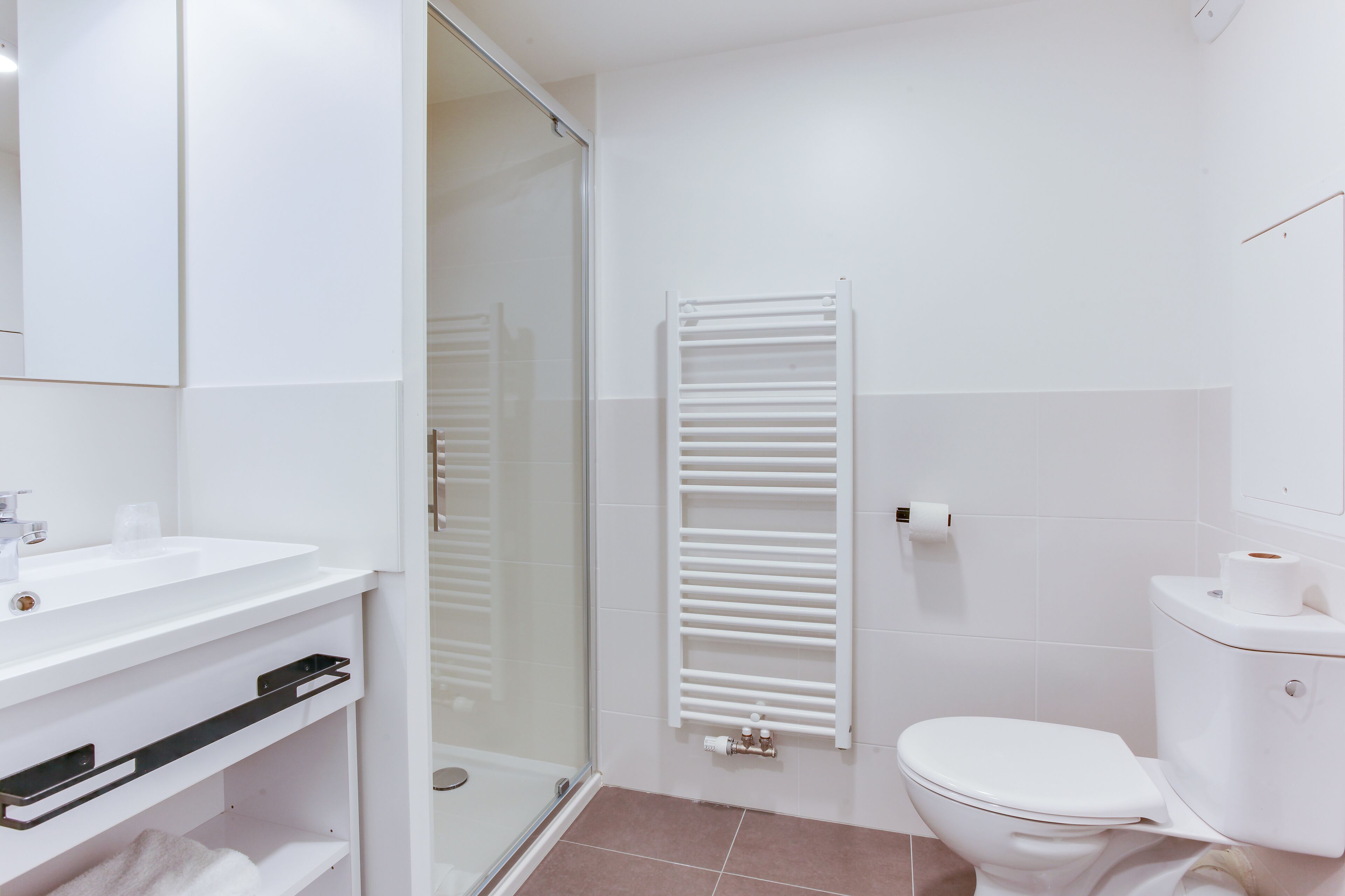A modern bathroom with a glass shower enclosure, a white toilet, and a towel rack.