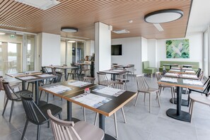 A modern dining area with multiple tables and chairs, a green sofa, and a large painting on the wall. - All Suites Appart Hôtel | Palaiseau - Massy TGV (Palaiseau)
