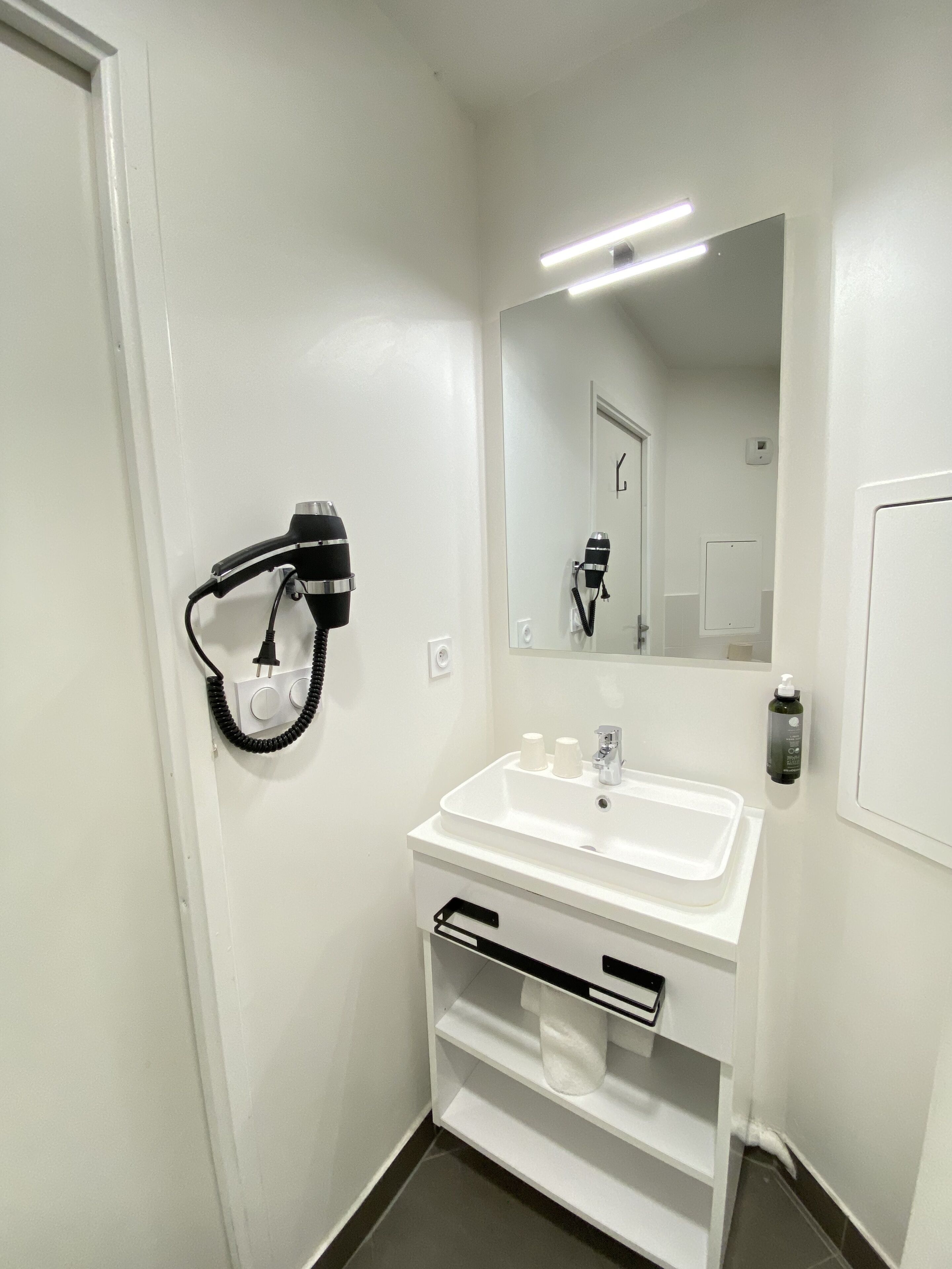 A small, clean bathroom with a white sink, a mirror, and a hairdryer on a wall-mounted stand.