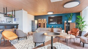 Un área de lounge moderna con bar, asientos y una pantalla de televisión grande.