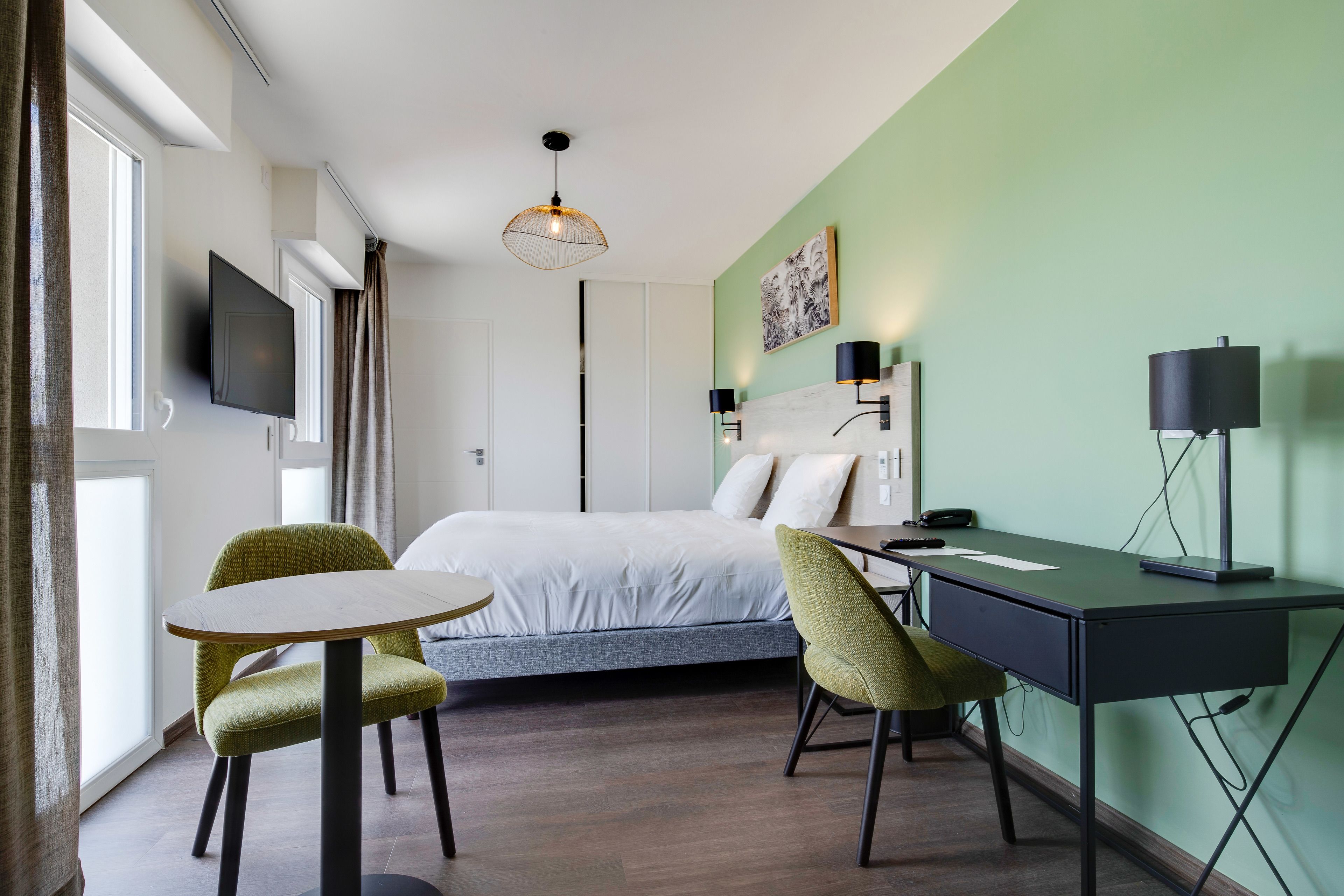 Una habitación de hotel moderna con una cama, dos sillones, un escritorio y un televisor.
