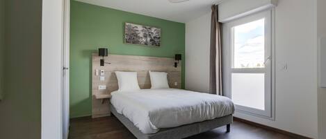 A bedroom with a bed, a headboard, a wall-mounted light, a window, and a door.