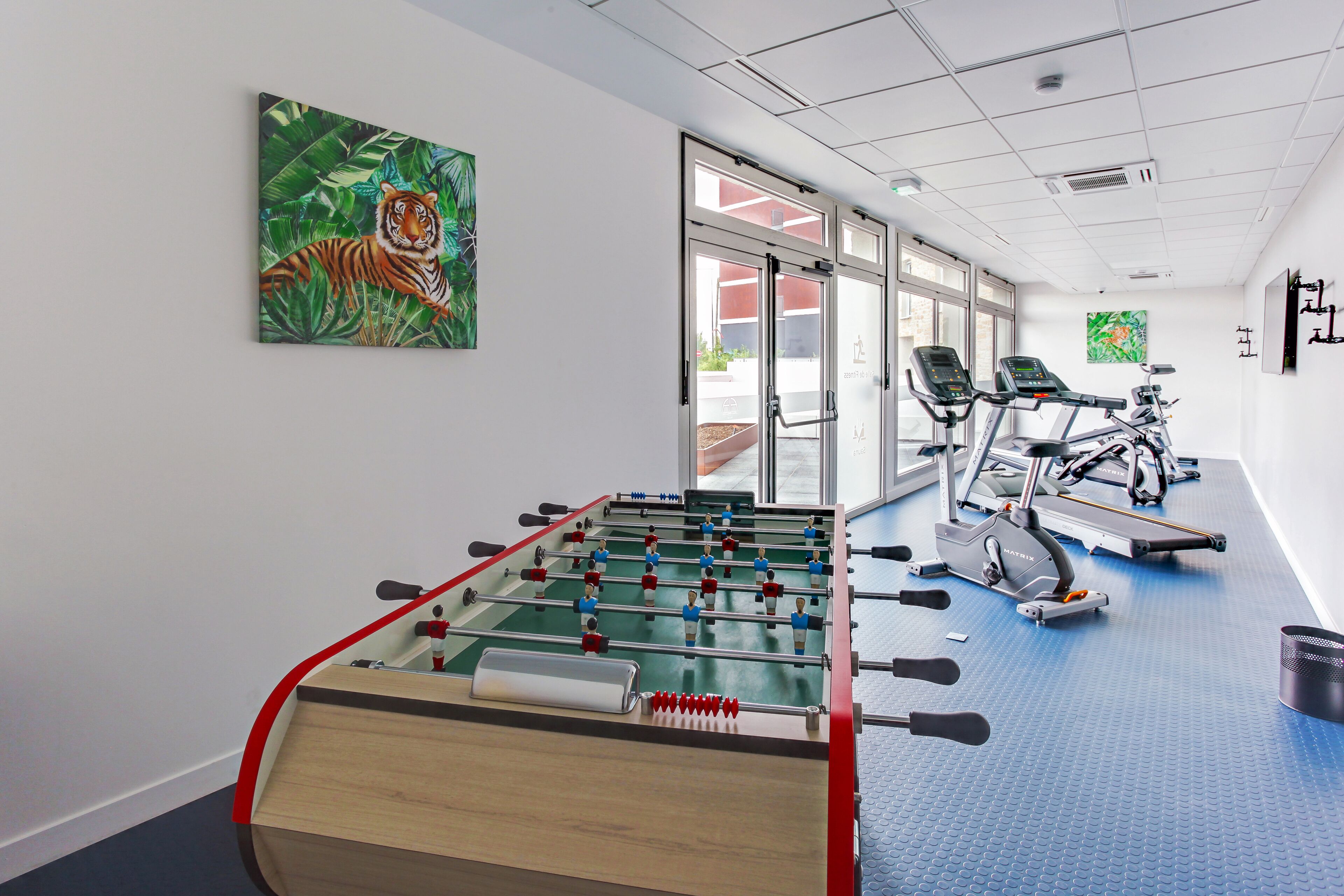 A room with a foosball table, exercise bikes, and a treadmill.