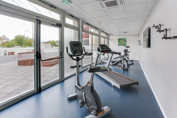 Un gimnasio con máquinas de cardio, ventanas amplias y suelo azul.