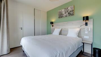 A neatly made bed in a room with a green wall, a wooden headboard, and two wall-mounted lamps.
