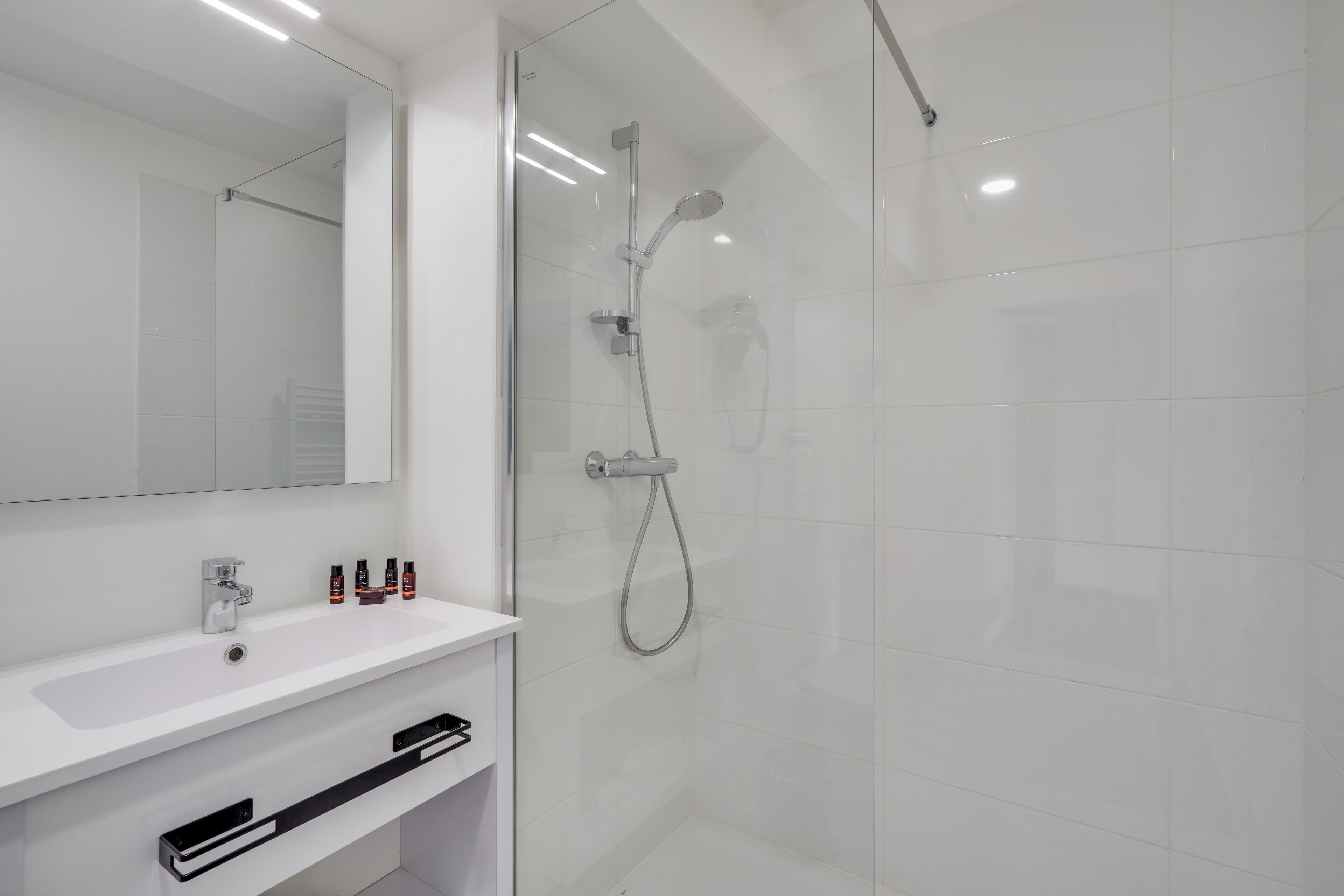 Un baño moderno con ducha de vidrio, un lavamanos blanco y un espejo encima.