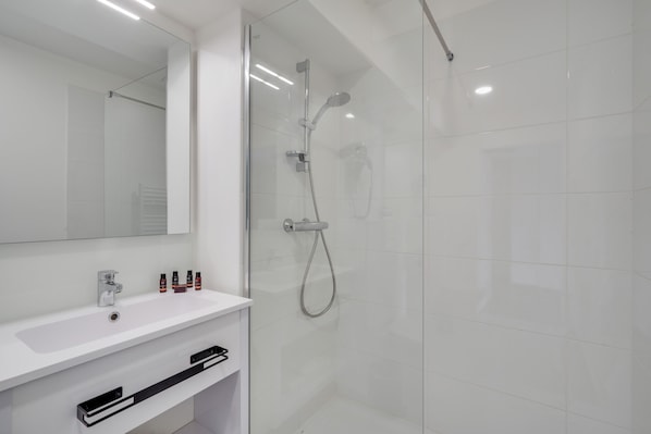 A modern bathroom with a glass-enclosed shower, a white sink, and a mirror above it. - All Suites Appart Hôtel | Palaiseau - Massy TGV (Palaiseau)