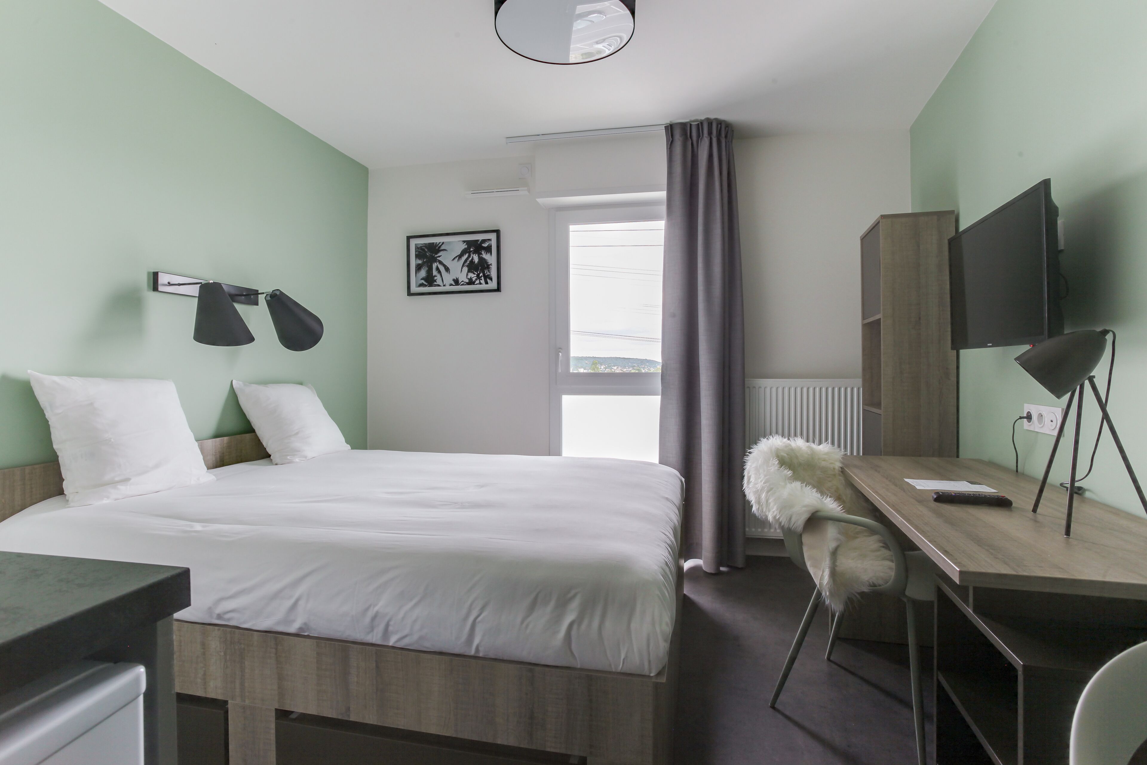 A hotel room with a bed, a desk, a chair, a TV, and a window with curtains.