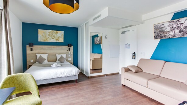 Una habitación de hotel moderna con una cama, un sofá, una silla y un espejo grande.