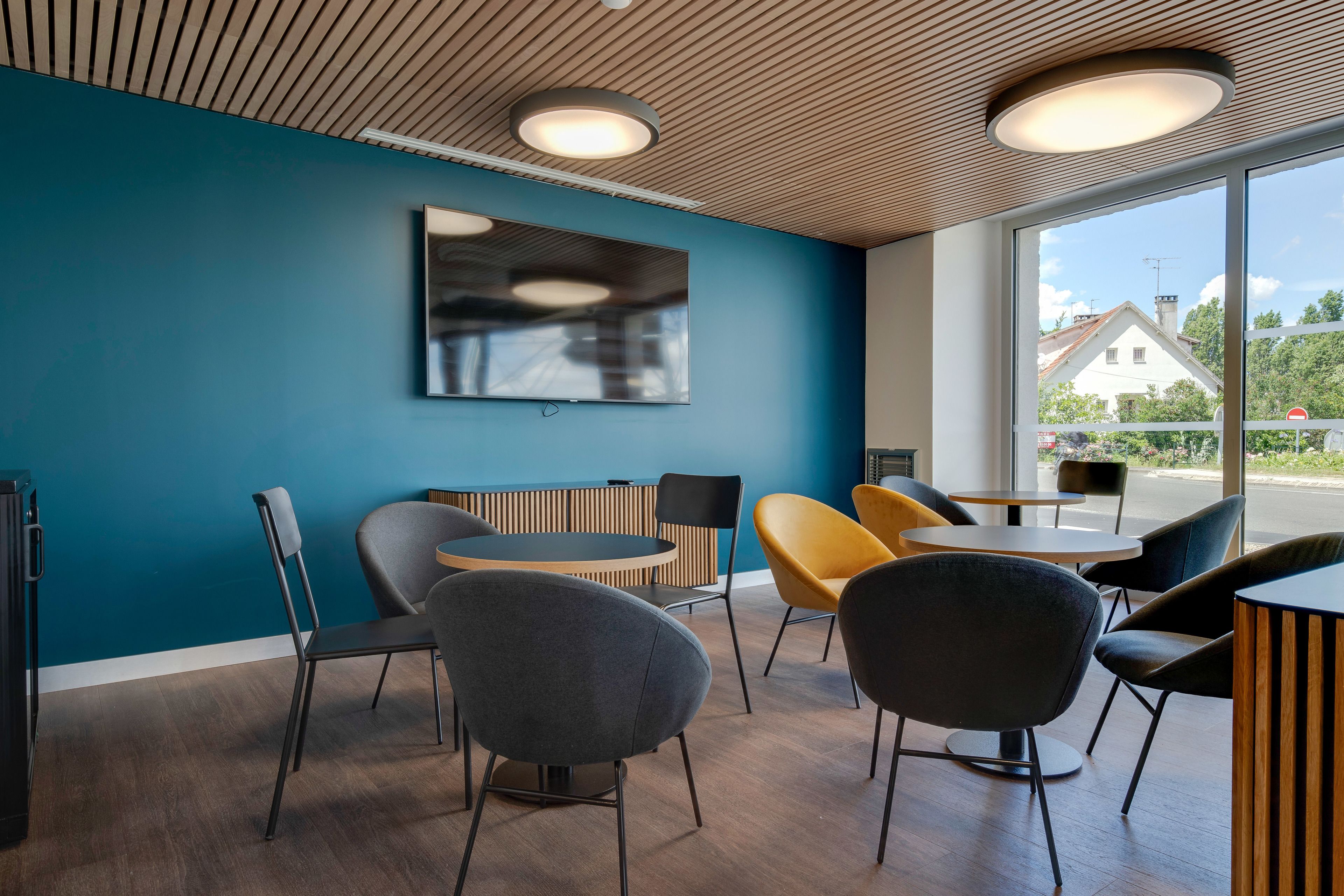 A modern interior with a blue wall, wooden ceiling, and large windows offering a view of the outside.