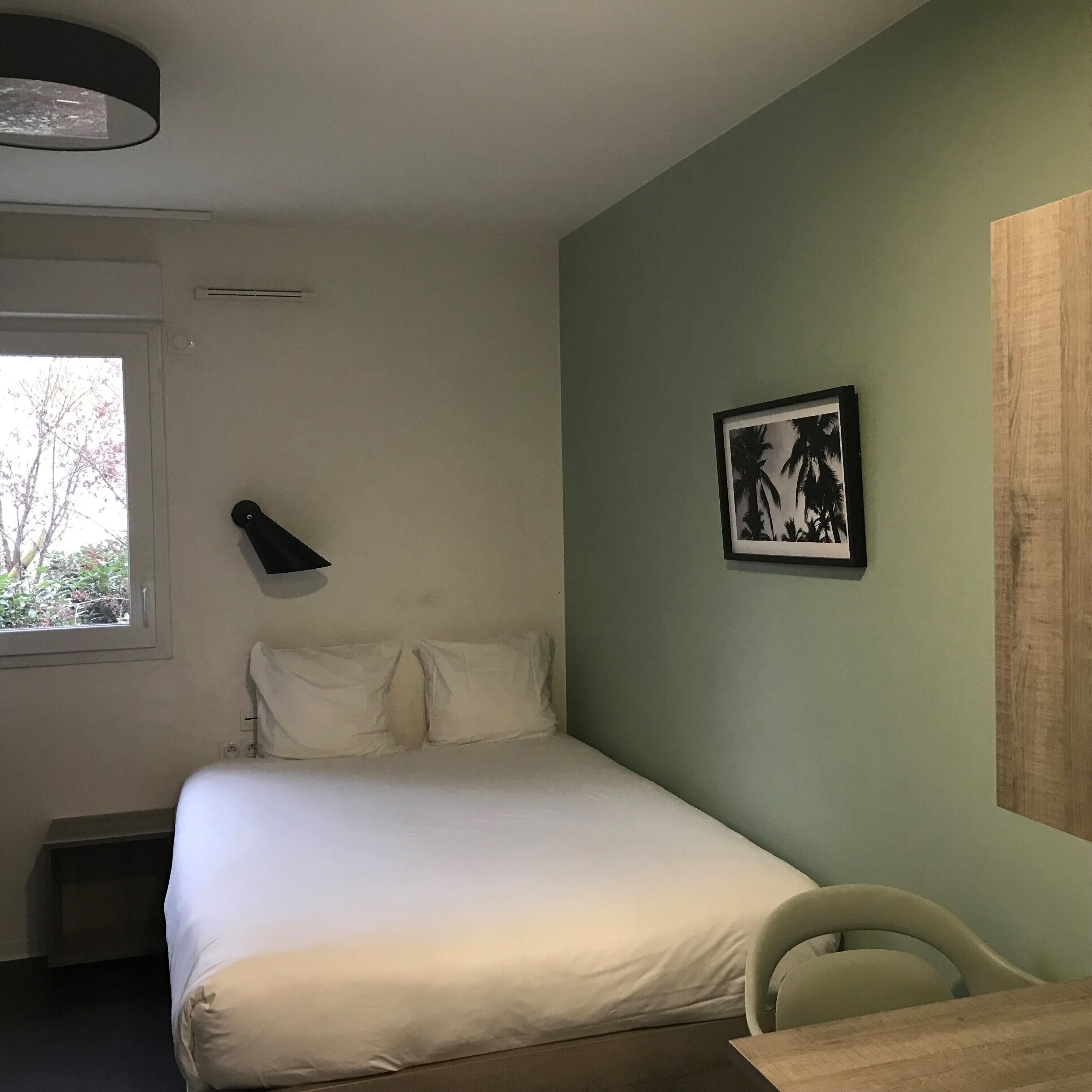 A bedroom with a bed, a desk, a chair, a window, and a framed picture on the wall.