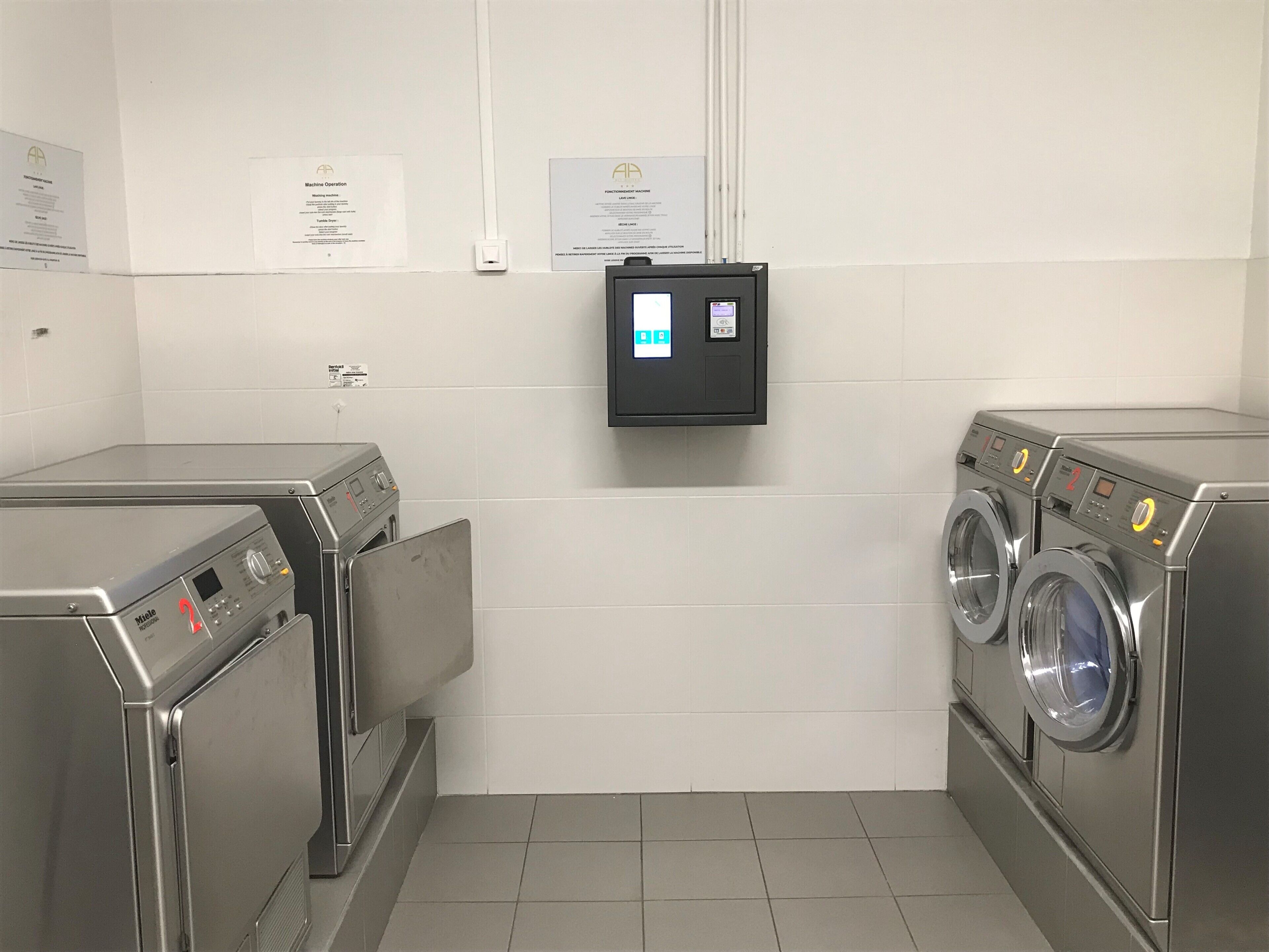 Ein Waschraum mit zwei Waschmaschinen mit Frontlader, einer Steuerungstafel und Hinweisschildern an der Wand.