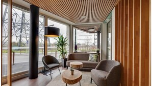 Un interior moderno con techo de madera, ventanas amplias, un sofá, dos sillones, una mesita redonda y una planta en maceta.