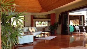 A spacious living area with a wooden ceiling, a sofa, a coffee table, and a dining area with chairs. - Absolute Beachfront Fiji (Nadi)