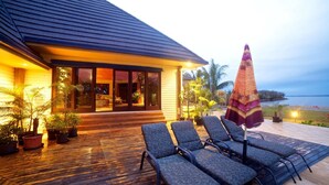 A modern house with a wooden deck, outdoor seating, and a view of the ocean. - Absolute Beachfront Fiji (Nadi)