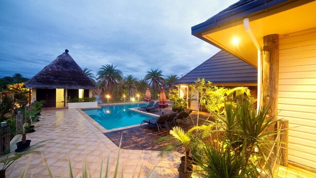 A swimming pool with lounge chairs, a thatched-roof structure, and tropical plants. - Absolute Beachfront Fiji (Nadi)