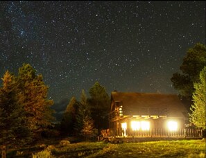 Una cabaña rústica con un cielo estrellado, rodeada de árboles.