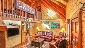 A log cabin interior with a wooden ceiling, a fireplace, a sofa, a coffee table, and a television. - Webb Cabin Mountain (Angel Fire)
