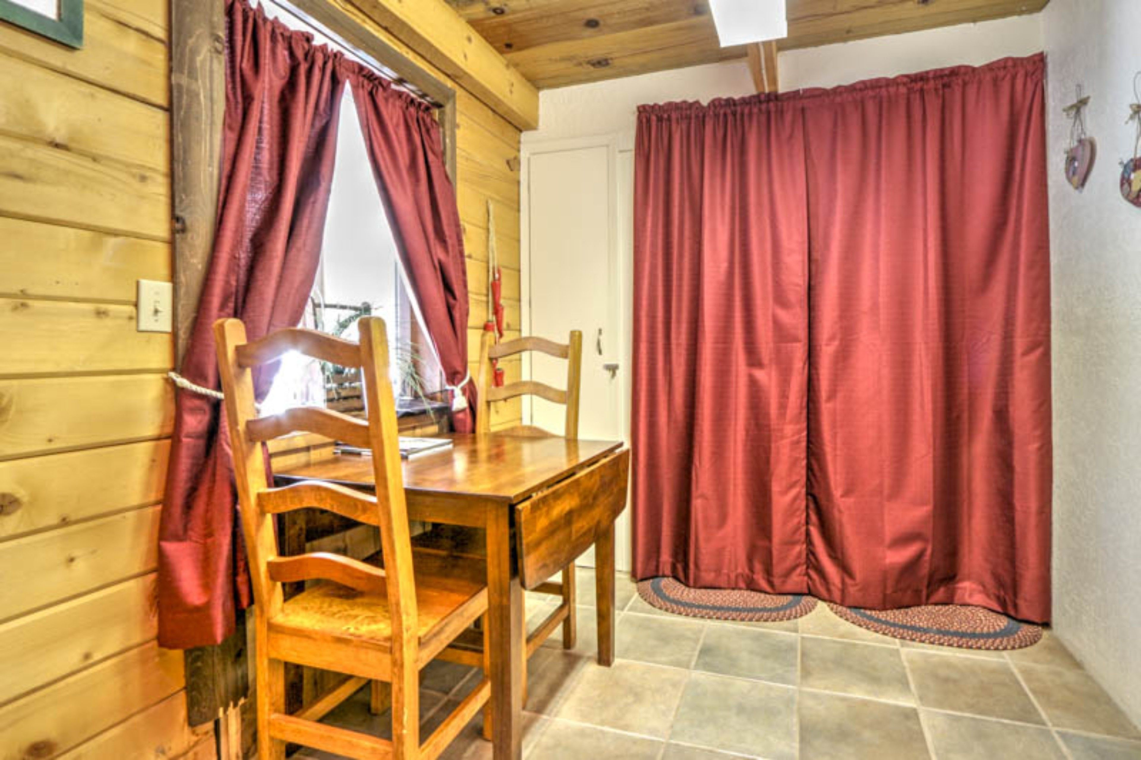 A wooden interior with a dining table and chairs, red curtains, and a tiled floor.