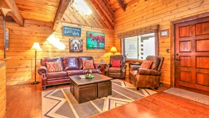A log cabin interior with a wooden ceiling, a leather sofa, a coffee table, and a door. - Webb Cabin Mountain (Angel Fire)