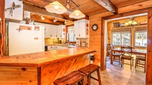 A rustic kitchen with wooden cabinets, a large wooden island, and hanging pendant lights. - Webb Cabin Mountain (Angel Fire)