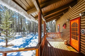 A wooden cabin with a porch, a red door, and a view of a snowy forest. - Webb Cabin Mountain (Angel Fire)