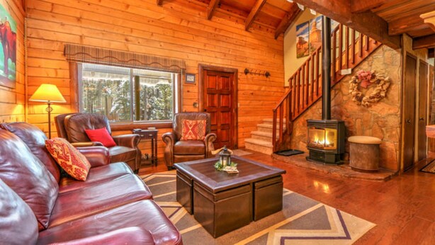 A cozy log cabin interior with leather furniture, a fireplace, and a staircase leading to an upper level. - Webb Cabin Mountain (Angel Fire)