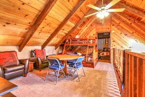 A cozy attic room with a wooden ceiling, a bunk bed, a dining table with chairs, and a leather sofa. - Webb Cabin Mountain (Angel Fire)