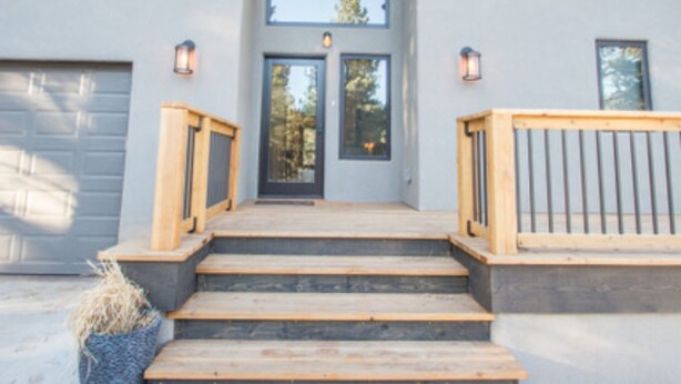 A modern house with a wooden staircase leading to a dark entrance, a covered porch, and a garage. - Lucky 8 Luxury Home (Angel Fire)