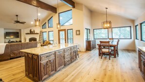 A spacious kitchen with wooden cabinets, a large island, and a dining area with chairs. - Lucky 8 Luxury Home (Angel Fire)