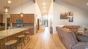 A spacious kitchen with wooden cabinets, a large island with stools, and pendant lighting. - Lucky 8 Luxury Home (Angel Fire)