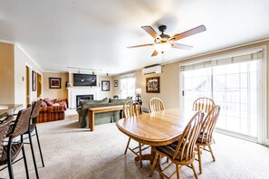 A spacious living room with a wooden dining table, comfortable seating, a fireplace, and large windows.