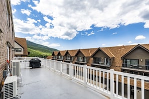 A row of modern, two-story buildings with a white fence in the foreground, a clear sky, and a mountain in the background.