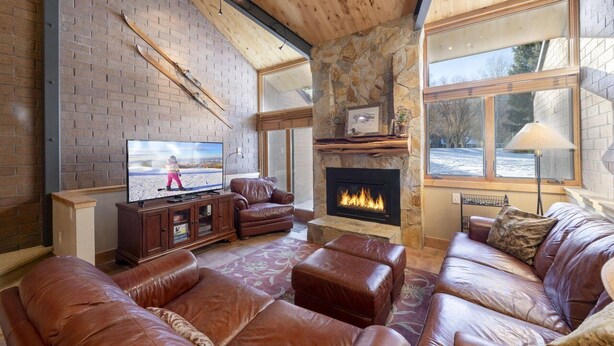 A cozy living room with a fireplace, leather sofas, a television, and a stone wall.