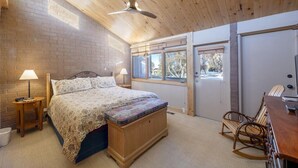 A bedroom with a bed, bedside lamps, a wooden bench, a rocking chair, and a ceiling fan.