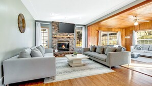 A modern living room with a fireplace, two sofas, a coffee table, and large windows.